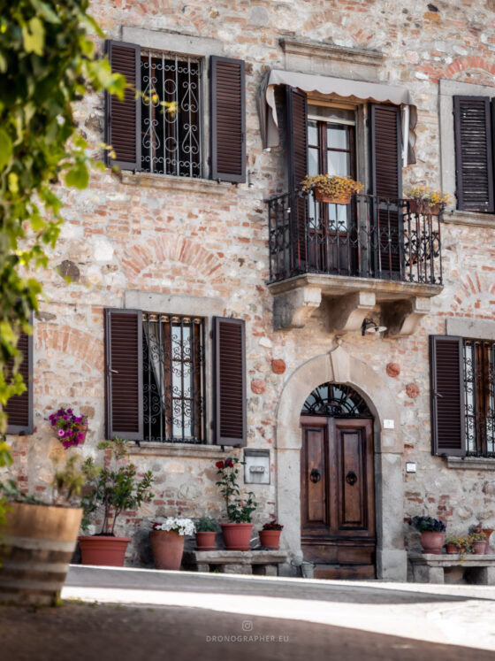 A house with typical tuscan architecture, a wooden door, a little balcony and flowers along the wall.