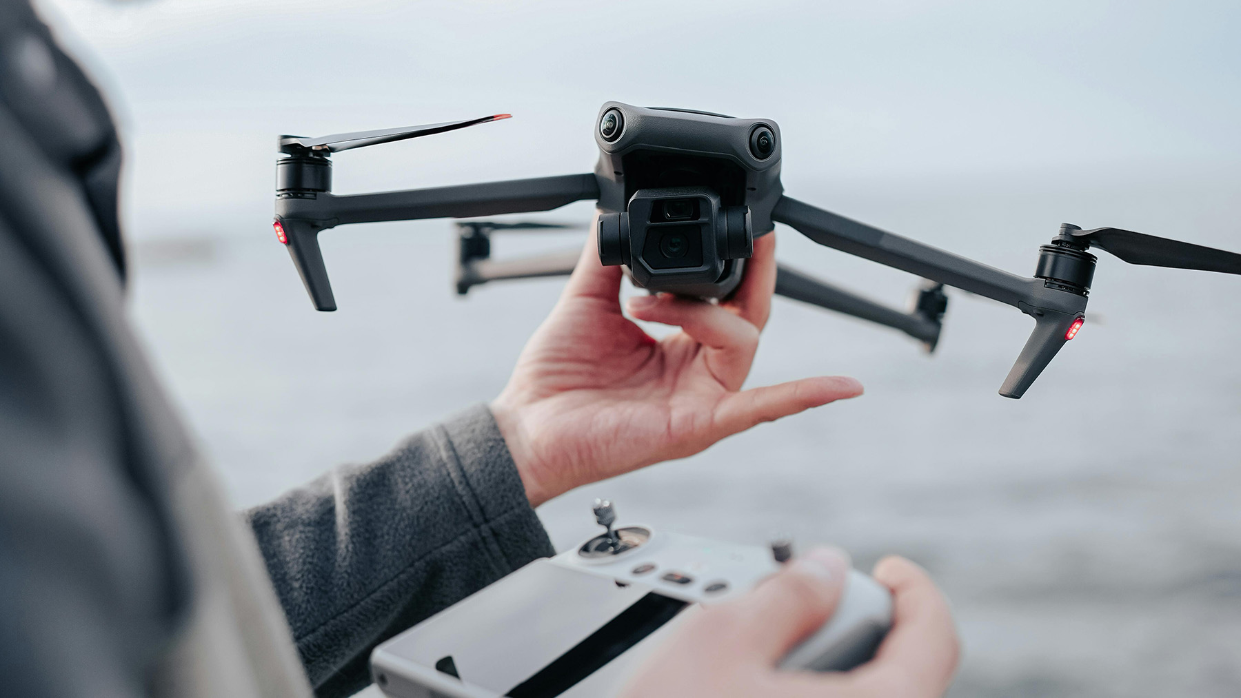 A person holding a medium-sized drone (DJI Mavic 3) in their hand, ready to start it with the RC controller in the other hand.